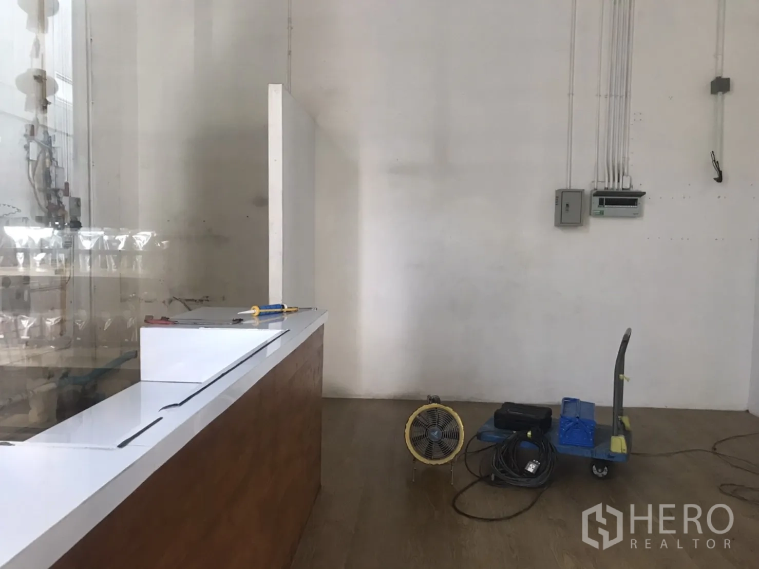 零售空间 出租在Khlong Toei, Bangkok - 小型零售铺面内景，白色墙面、木纹地板、白色服务台与电箱设备。