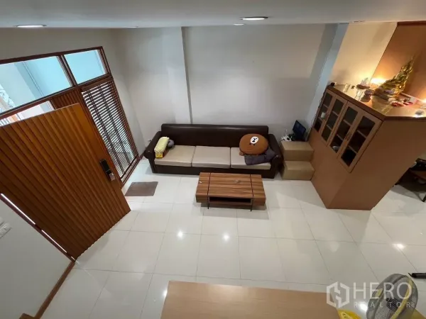 Townhouse for rent in Bang Kho Laem, Bangkok - View from staircase over living room with sofa, coffee table, and wood screen.