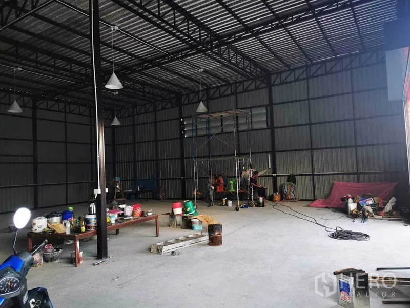 Warehouse for rent - Interior corner with scaffolding and tools beneath a high steel roof and open concrete floor.