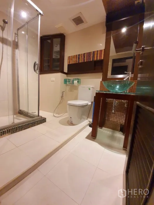Condominium for rent or sale in Pathum Wan, Bangkok - Main bathroom with glass-enclosed shower, vessel sink on tiled vanity and toilet.