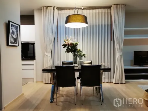 公寓 出售在Bangkok - 正面视角的餐桌与大吊灯，左右为小厨房与电视收纳墙。