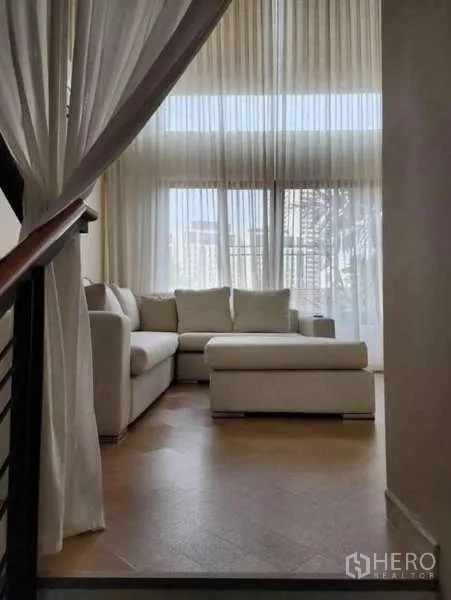 Townhouse for rent - Bright double-height living room with a white sectional sofa and sheer floor-to-ceiling curtains.
