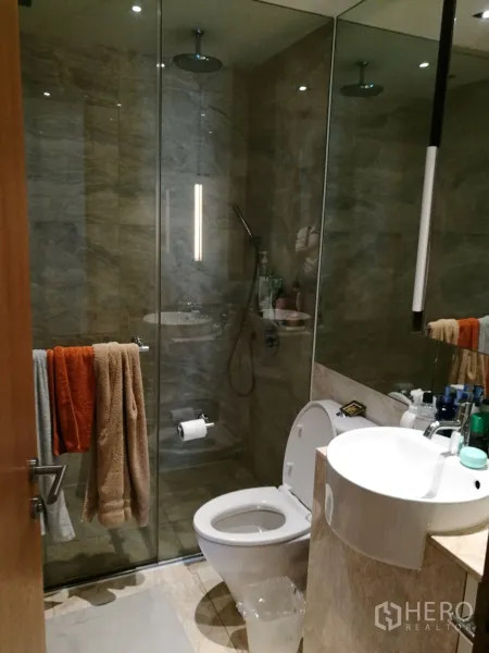 Condominium for rent or sale in Sathon, Bangkok - Modern bathroom featuring a glass walk-in shower with rain showerhead and vanity sink.