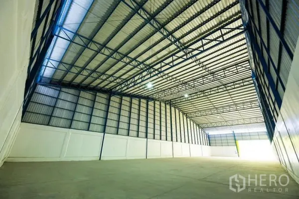 Warehouse for rent in Phra Phutthabat, Saraburi - High-clearance warehouse interior showing steel truss roof, skylights, and smooth concrete floor.