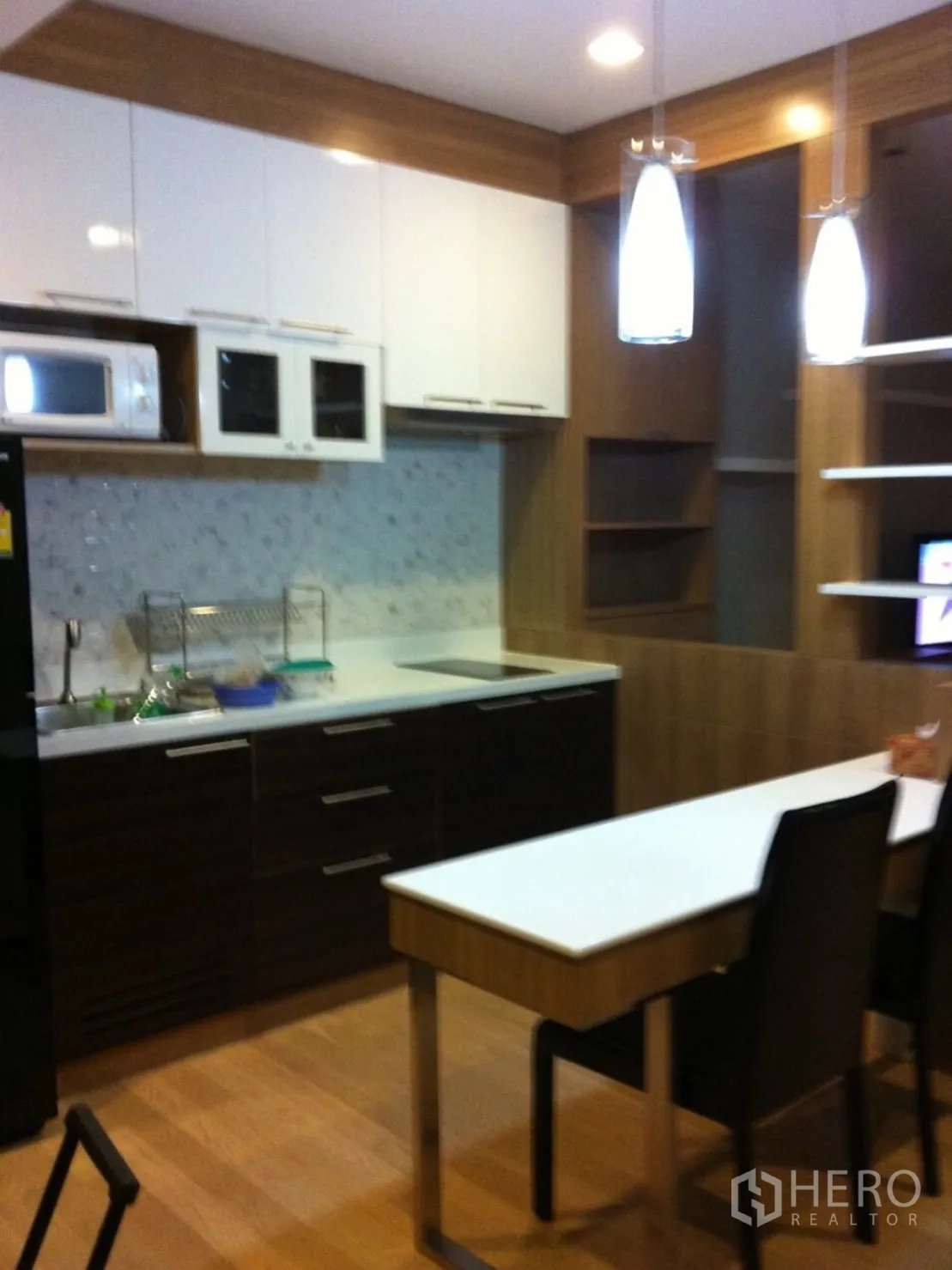 Condominium for rent or sale in Watthana, Bangkok - Modern Ekkamai condo kitchen with white wall cabinets, dark wood base units, pendant lights and a breakfast counter.