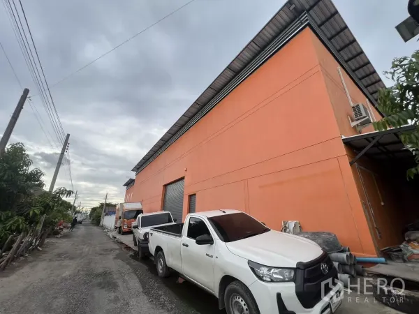 คลังสินค้า ให้เช่าหรือขายในLat Krabang, Bangkok - มุมข้างอาคารโกดังสีส้มติดซอยแคบ มีรถกระบะจอดและพื้นที่ขนถ่าย