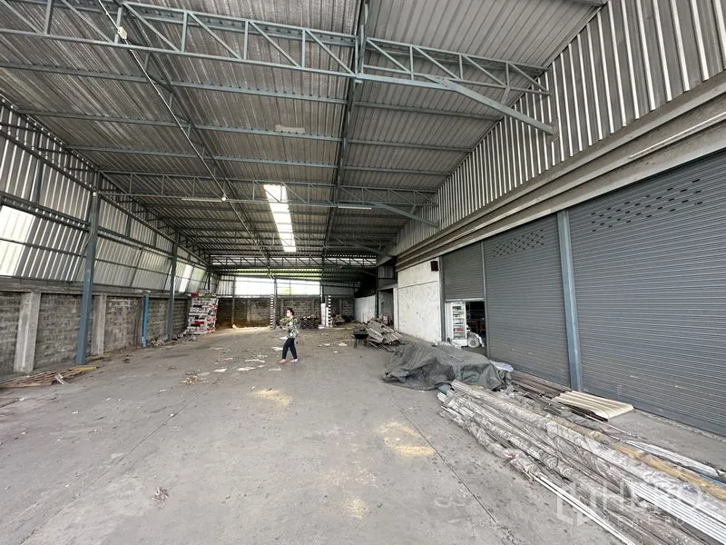 Warehouse for sale in Bang Khen, Bangkok - Open storage hall with high ceiling and side roller shutters along the wall.