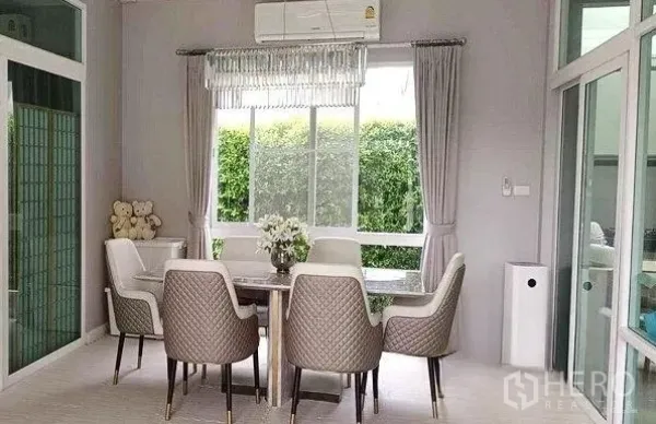 Detached House for rent in Don Mueang, Bangkok - Bright dining area with a six-seat table, chandelier and a large window facing green hedges.