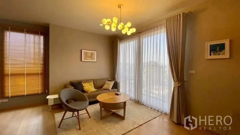 Condominium for rent or sale in Watthana, Bangkok - Living room with full-height sliding doors to the balcony and warm ambient lighting.