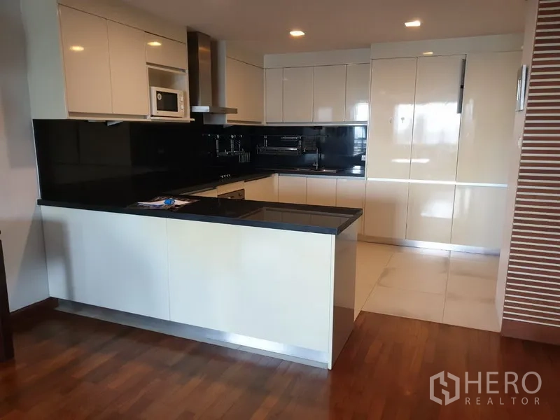 Condominium for rent in Watthana, Bangkok - Modern white kitchen with black stone countertops, island breakfast bar and built-in appliances.