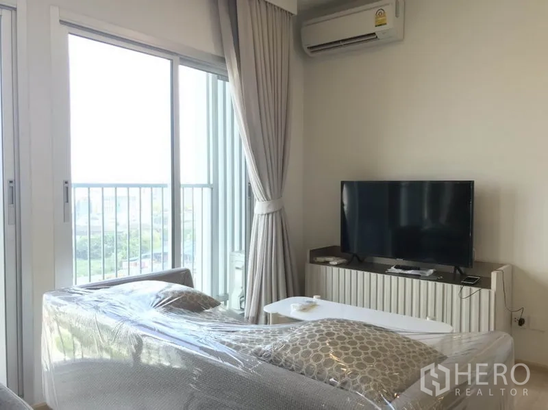 คอนโด ให้เช่าในHuai Khwang, Bangkok - พื้นที่นั่งเล่นติดประตูระเบียง วิวเมือง มีตู้วางทีวีและเครื่องปรับอากาศ