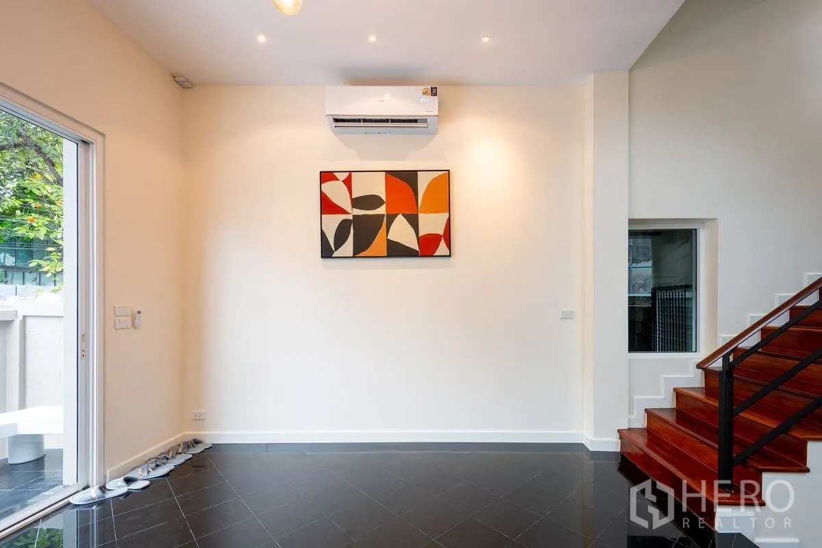 Detached House for rent or sale in Chatuchak, Bangkok - Bright entry room with wall-mounted air conditioner, abstract art, black tile floor, and wooden stairs.