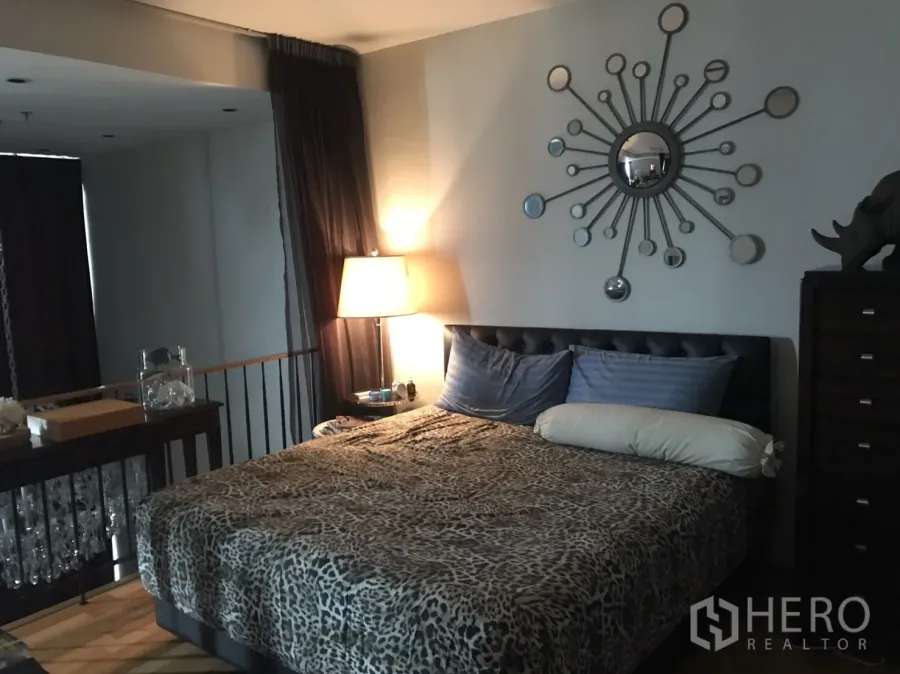 คอนโด ให้เช่าหรือขายในKhlong Toei, Bangkok - ห้องนอนหลักพร้อมหัวเตียงบุ หนัง กระจกตกแต่งซันเบิร์สต์ โคมไฟข้างเตียง และผ้าม่านทึบ