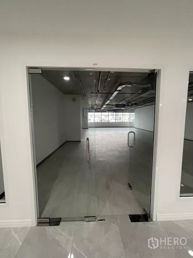 办公空间 出租在Bang Rak, Bangkok - 玻璃双开门通向明亮的开放式办公区，灰色地面与整面窗户。