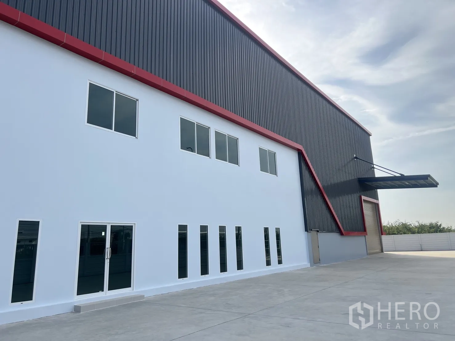 คลังสินค้า ให้เช่าในMueang Samut Prakan, Samut Prakan - ภาพระยะใกล้ด้านหน้าออฟฟิศ 2 ชั้นสีขาวติดกับโกดัง พร้อมถนนทางเข้าและกันสาดโหลดสินค้า