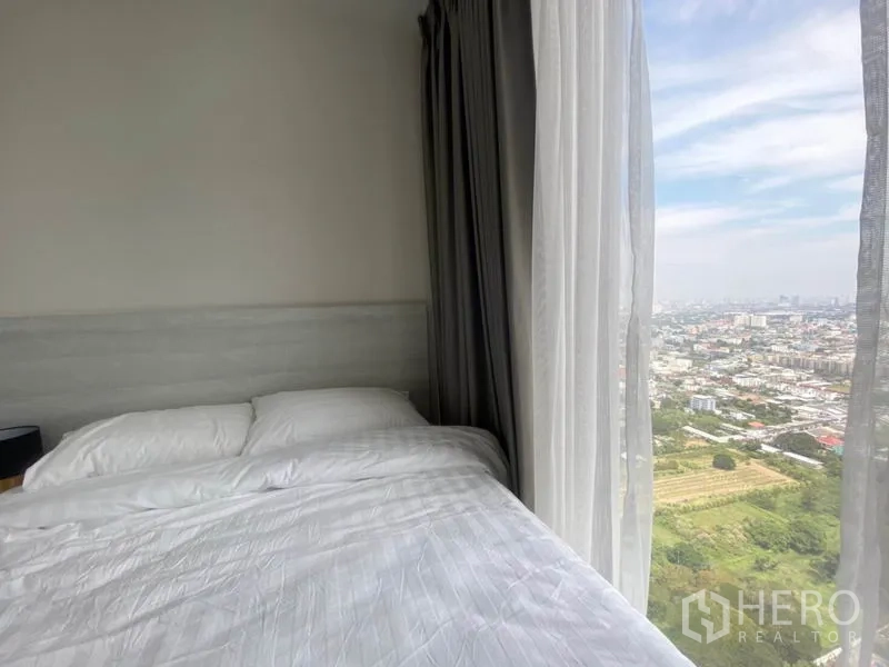 Condominium for rent in Phra Khanong, Bangkok - Corner bedroom view with bed next to panoramic window showcasing Bangkok skyline and greenery.