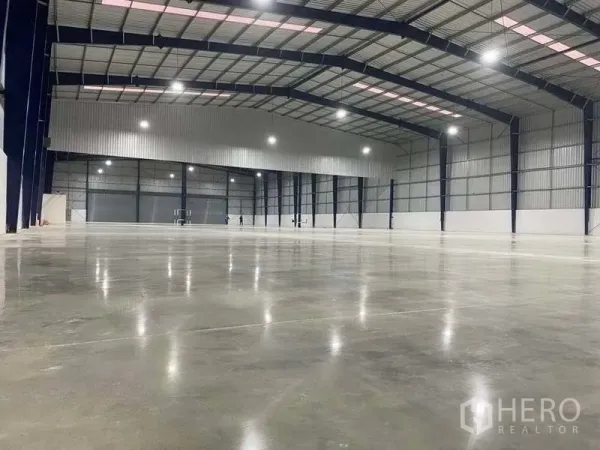 Warehouse for rent in Nonthaburi - Spacious clear‑span warehouse interior with polished concrete floor, high steel roof, and bright lighting.