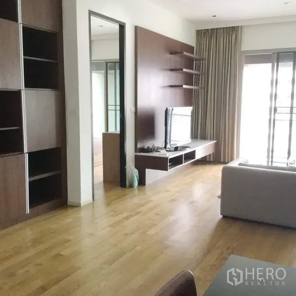 คอนโด ให้เช่าในWatthana, Bangkok - ห้องนั่งเล่นพื้นไม้ มีชั้นวางทีวีและชั้นบิวท์อิน ผนังตกแต่งไม้ พร้อมประตูกระจกบานเลื่อนออกไประเบียง