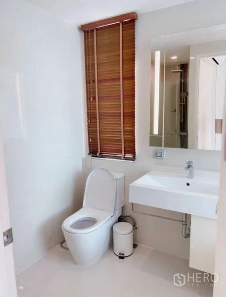 Condominium for rent in Watthana, Bangkok - Bathroom with window blinds, toilet and wide mirror above the sink.