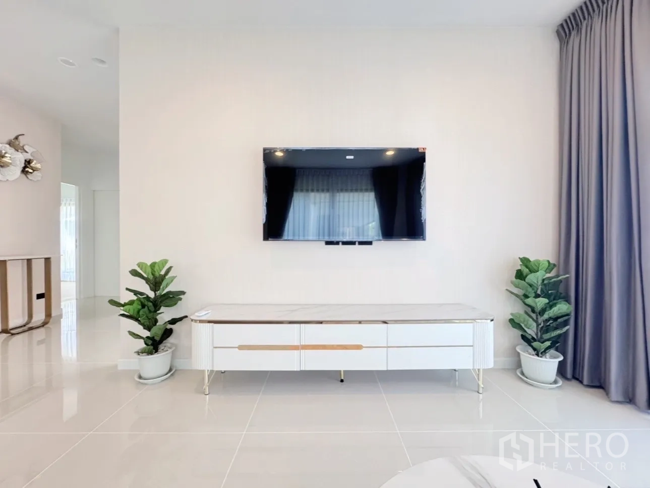 บ้าน ให้เช่าหรือขายในBang Kapi, Bangkok - ผนังทีวีพร้อมตู้คอนโซลและกระถางต้นไม้ ในห้องนั่งเล่นสว่างโล่ง