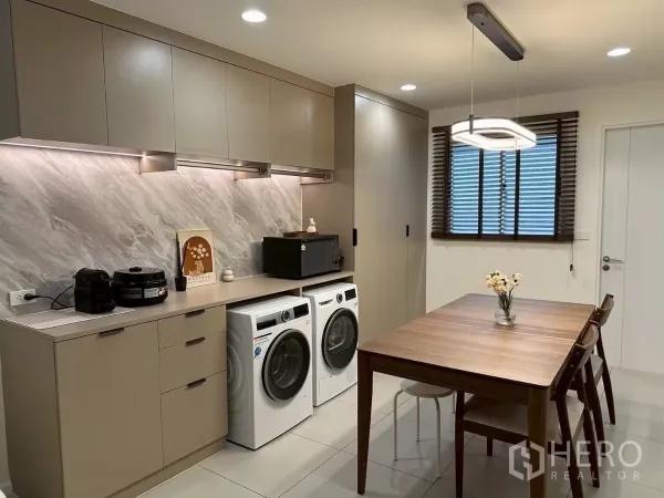 Townhouse for rent in Saphan Sung, Bangkok - Built-in pantry with marble-look backsplash, upper cabinets, and side-by-side washer and dryer next to the dining table.