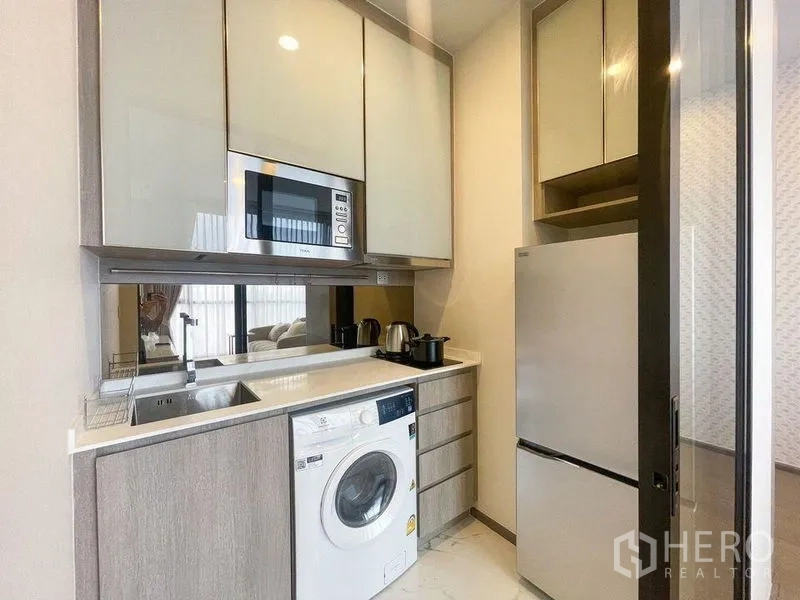 Condominium for rent in Ratchathewi, Bangkok - Compact kitchenette with microwave, sink, cooktop, washing machine and upper cabinets.