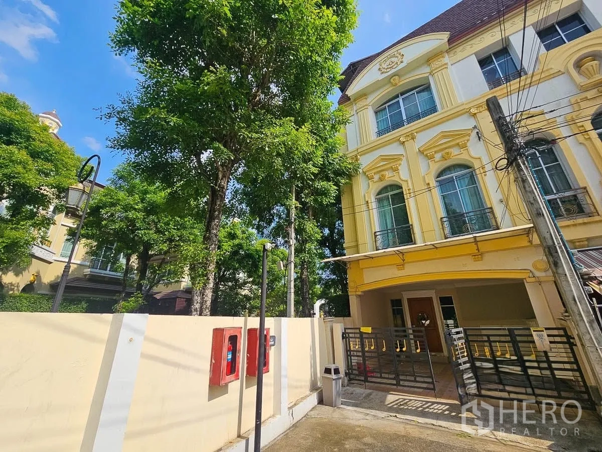 联排别墅 for rent in Yan Nawa, Bangkok - 角落联排外观，黄色立面，带大门车棚与成树。