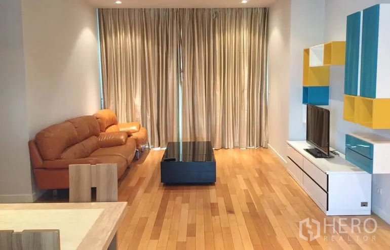 คอนโด ขายในKhlong Toei, Bangkok - ห้องนั่งเล่นสว่าง โซฟาหนังสีน้ำตาล ผ้าม่านสูงจรดเพดาน ตู้ทีวี และพื้นไม้