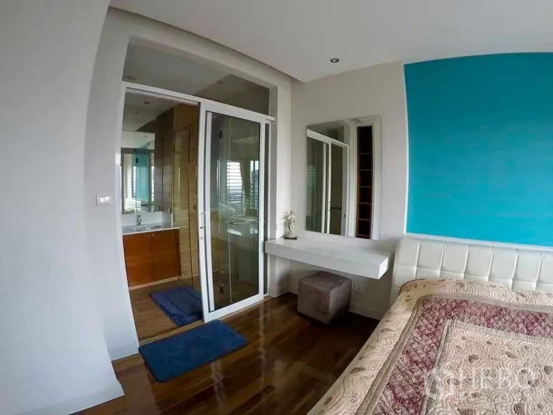 Condominium for rent or sale in Khlong San, Bangkok - Bedroom with blue accent wall, vanity desk and sliding door to an ensuite bathroom.