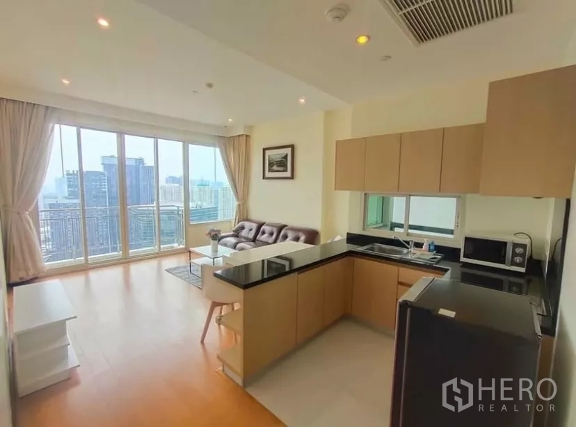 Condominium for rent in Chatuchak, Bangkok - Bright open-plan living room with corner kitchen and floor-to-ceiling windows overlooking the Chatuchak skyline.