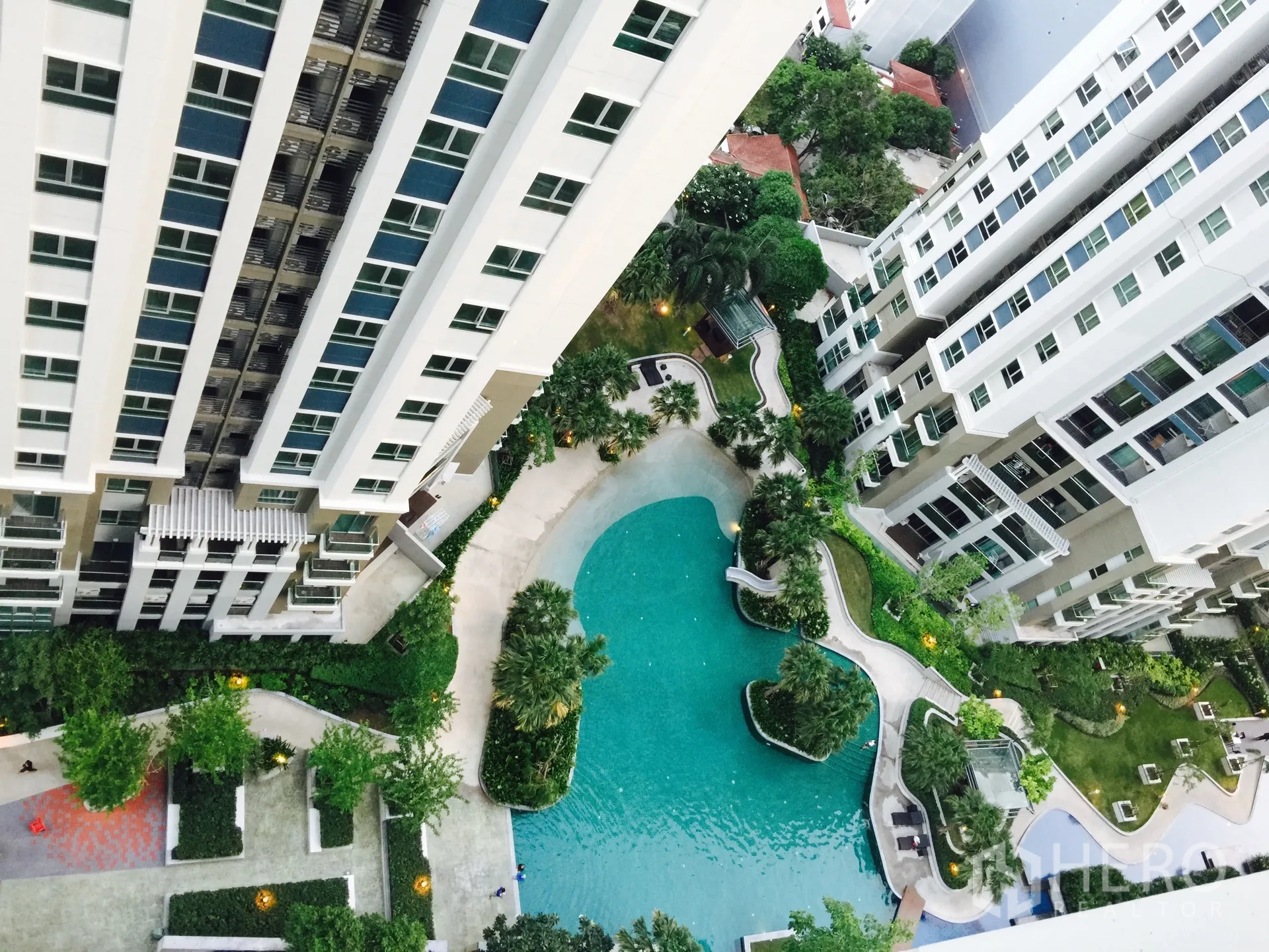 Condominium for rent in Huai Khwang, Bangkok - High-angle view of condominium towers with a resort-style lagoon swimming pool and landscaped gardens.