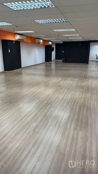 สำนักงาน ให้เช่า - โซนทำงานโล่ง มีคานสีส้ม แอร์ติดผนังหลายเครื่อง และพื้นไม้ลามิเนต