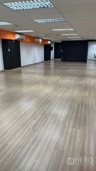 สำนักงาน ให้เช่า - โซนทำงานโล่ง มีคานสีส้ม แอร์ติดผนังหลายเครื่อง และพื้นไม้ลามิเนต