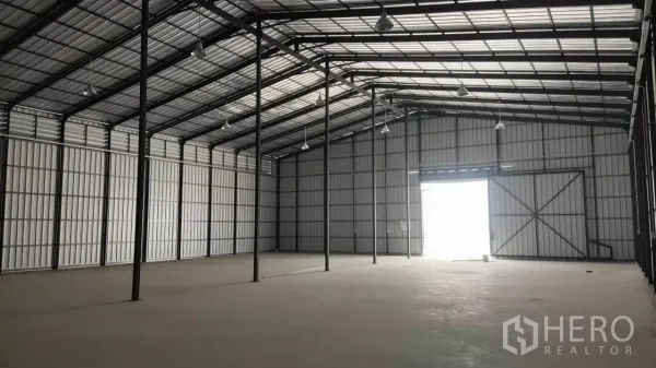 Warehouse for rent in Bang Lamung, Chon Buri - Spacious high-ceiling warehouse interior with steel frame, hanging lights and concrete floor.