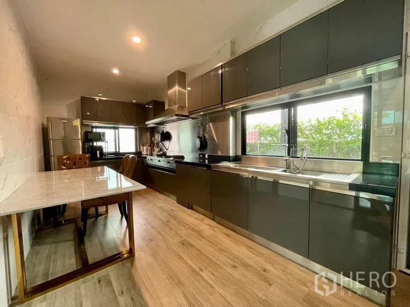 Detached House for rent in Phasi Charoen, Bangkok - Sleek galley kitchen with dark cabinets, range hood, and long countertop.