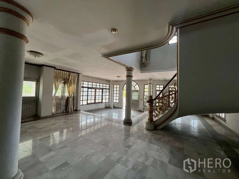 Detached House for rent in Prawet, Bangkok - Open‑plan hall with columns, many windows and a curved staircase.