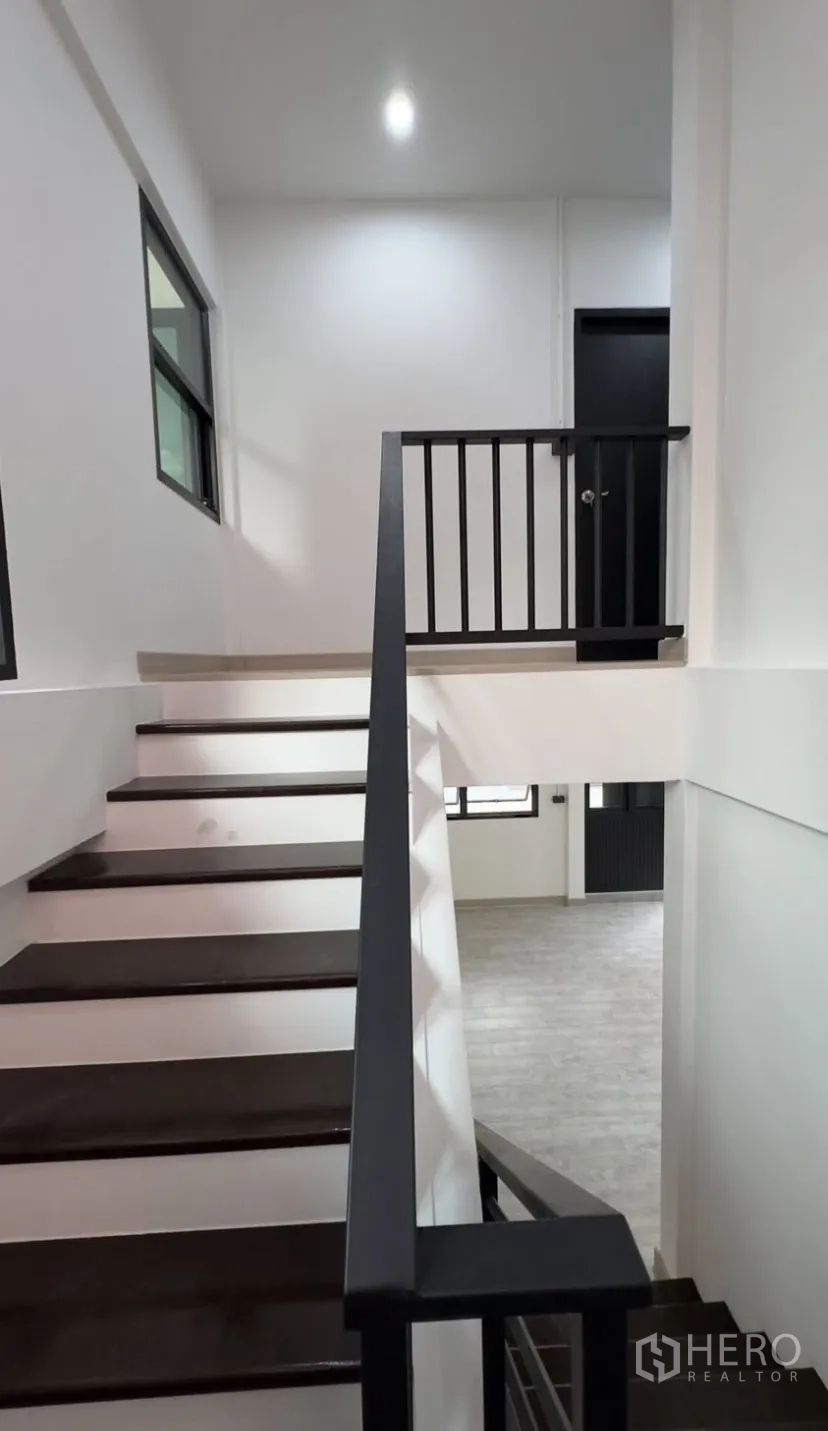Detached House for rent in Suan Luang, Bangkok - Staircase with dark timber steps and black metal railing in a bright hallway.