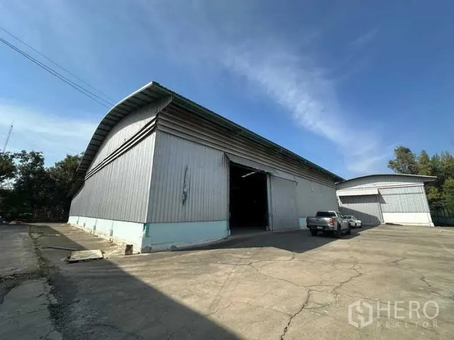 货栈 出租在Phra Nakhon Si Ayutthaya - 金属外墙仓库外观，拱形高屋顶与宽阔车道，晴朗蓝天下。