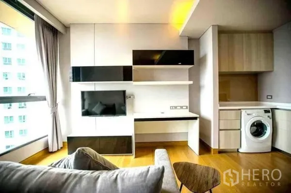 公寓 出租在Khlong Toei, Bangkok - 客厅设电视墙与书桌，开放式厨房配备洗衣机。