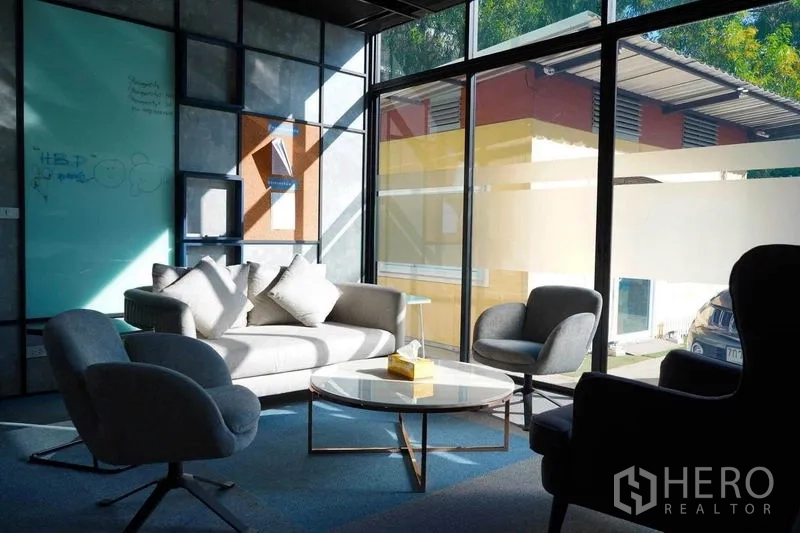 สำนักงาน ให้เช่าในBang Na, Bangkok - โซนนั่งเล่นรับแสงธรรมชาติ โซฟาสีเทา เก้าอี้เอนกประสงค์ และโต๊ะกลางทรงกลม