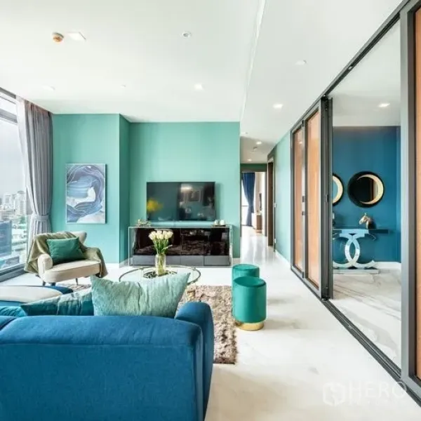 公寓 出租或出售在Watthana, Bangkok - 明亮客厅，青绿色墙面、电视柜、大窗与通往卧室的玻璃移门。