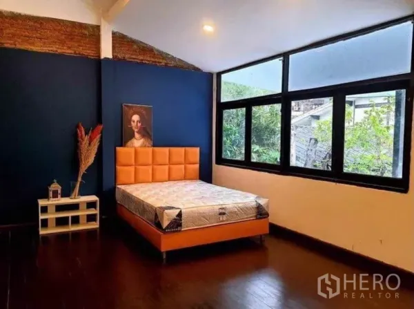 Detached House for rent in Pathum Wan, Bangkok - Spacious bedroom with large windows, deep blue accent wall and an orange upholstered bed.