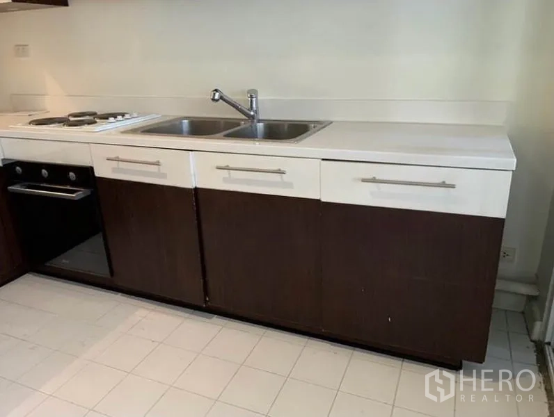 Townhouse for rent in Khlong Toei, Bangkok - Compact kitchen with white countertop, double sink, cooktop and built‑in oven.