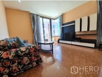 คอนโด ขาย - ห้องนั่งเล่นสว่างพร้อมโซฟาลายดอก ชุดผนังทีวี และประตูบานเลื่อนออกสู่ระเบียง