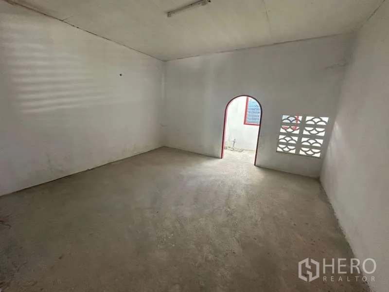 Warehouse for rent in Suan Luang, Bangkok - Simple spare room with arched doorway and breeze-block window providing ventilation.