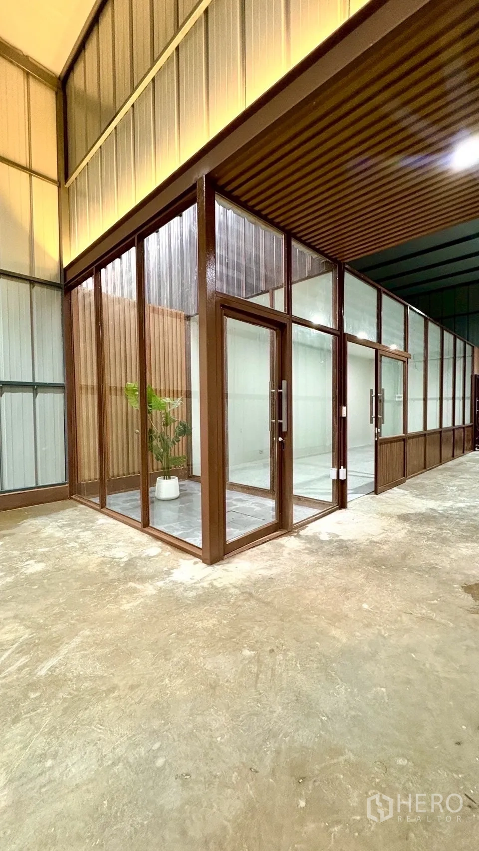 Warehouse for rent in Suan Luang, Bangkok - Corner glass office pod inside the warehouse with wood-tone frames and a potted plant.