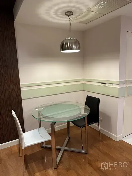 Condominium for rent in Watthana, Bangkok - Dining nook featuring a round glass table, two chairs and a metallic pendant lamp.