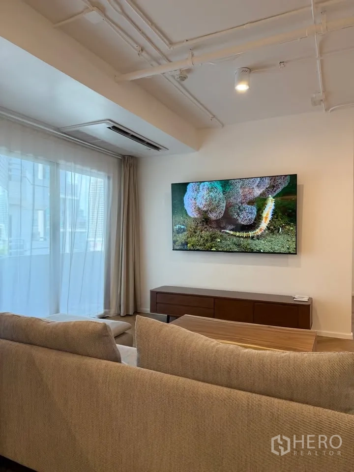 Condominium for rent in Watthana, Bangkok - Lounge with wall-mounted TV, media console, and sheer curtains.