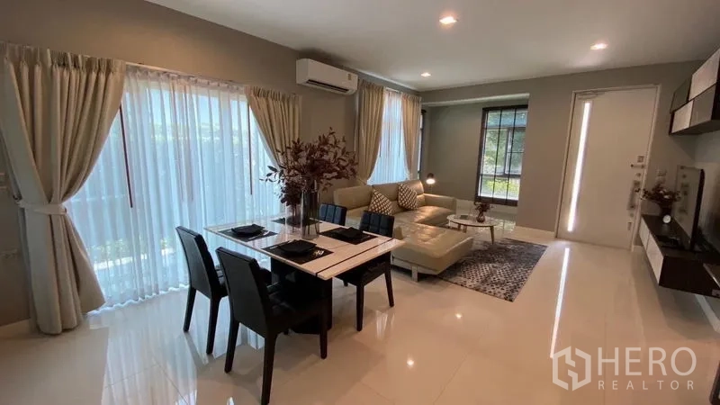 Detached House for rent in Samut Prakan - Bright open-plan lounge and dining space with glossy floors and full-height curtains.