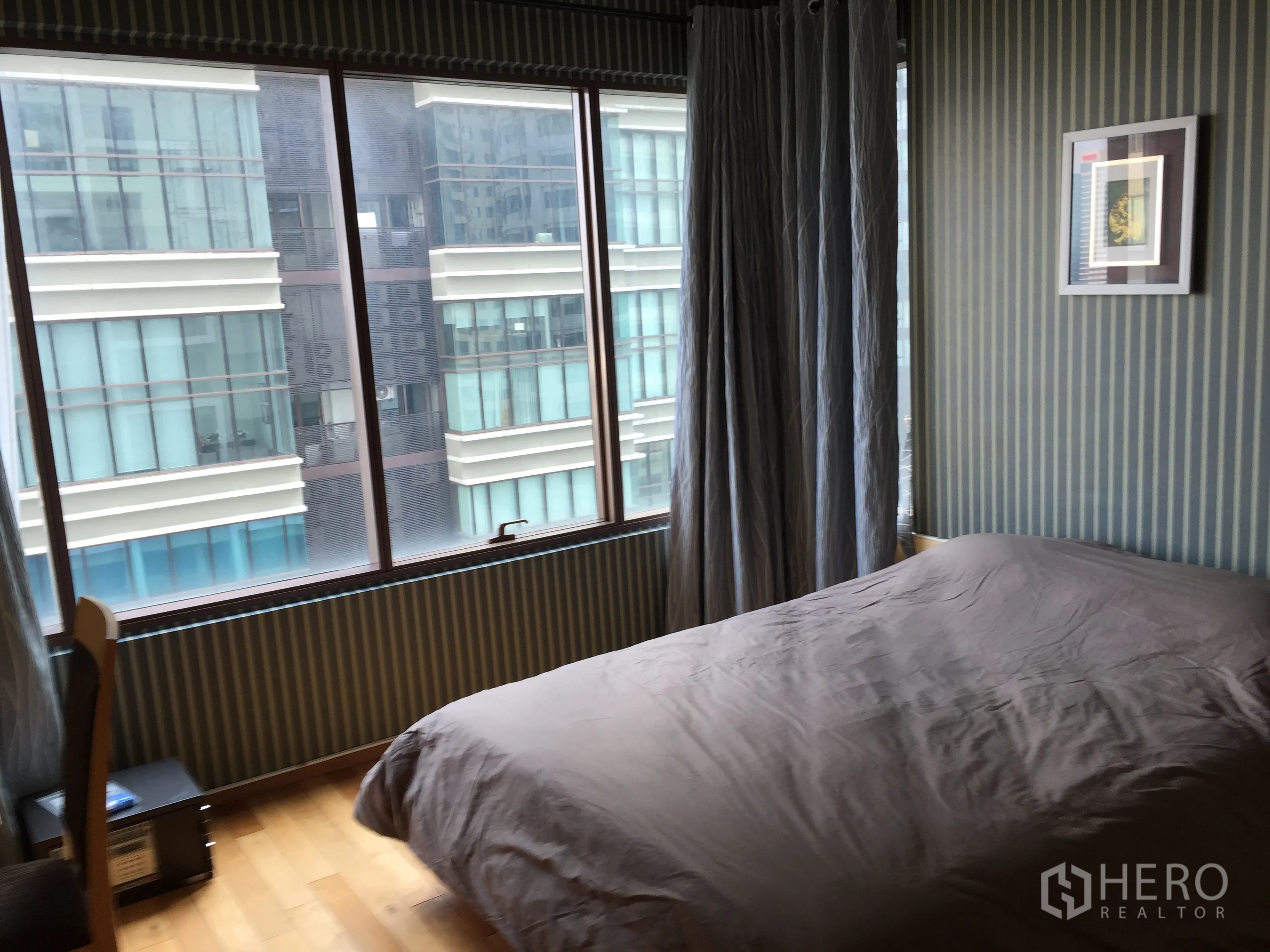 คอนโด ให้เช่าหรือขายในKhlong Toei, Bangkok - ห้องนอนมีหน้าต่างบานใหญ่ วอลเปเปอร์ลายทาง และวิวเมืองจากอาคารใกล้เคียง